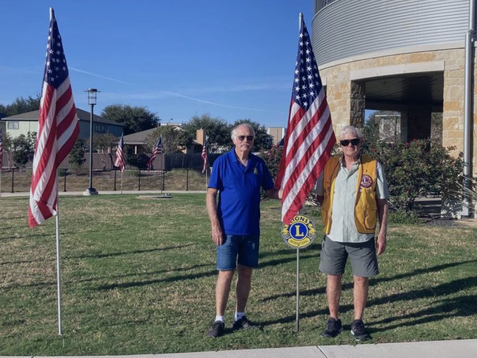 Two Lion Club members stand between flags on display