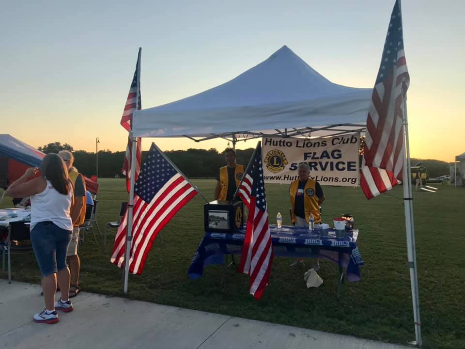 Two Hutto Lions Club members stand behind a booth surrounded by American flags